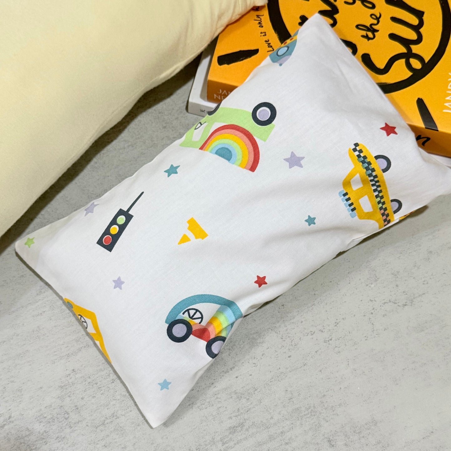 Husk pillow with colorful car, rainbow, and star designs on a gray surface.
