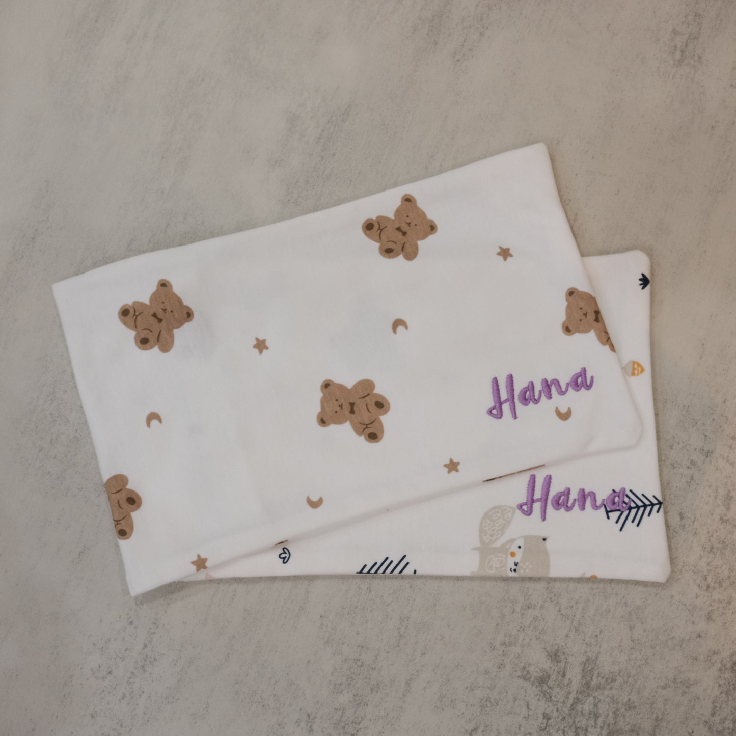 Two baby pillow cases with teddy bear patterns on a textured surface