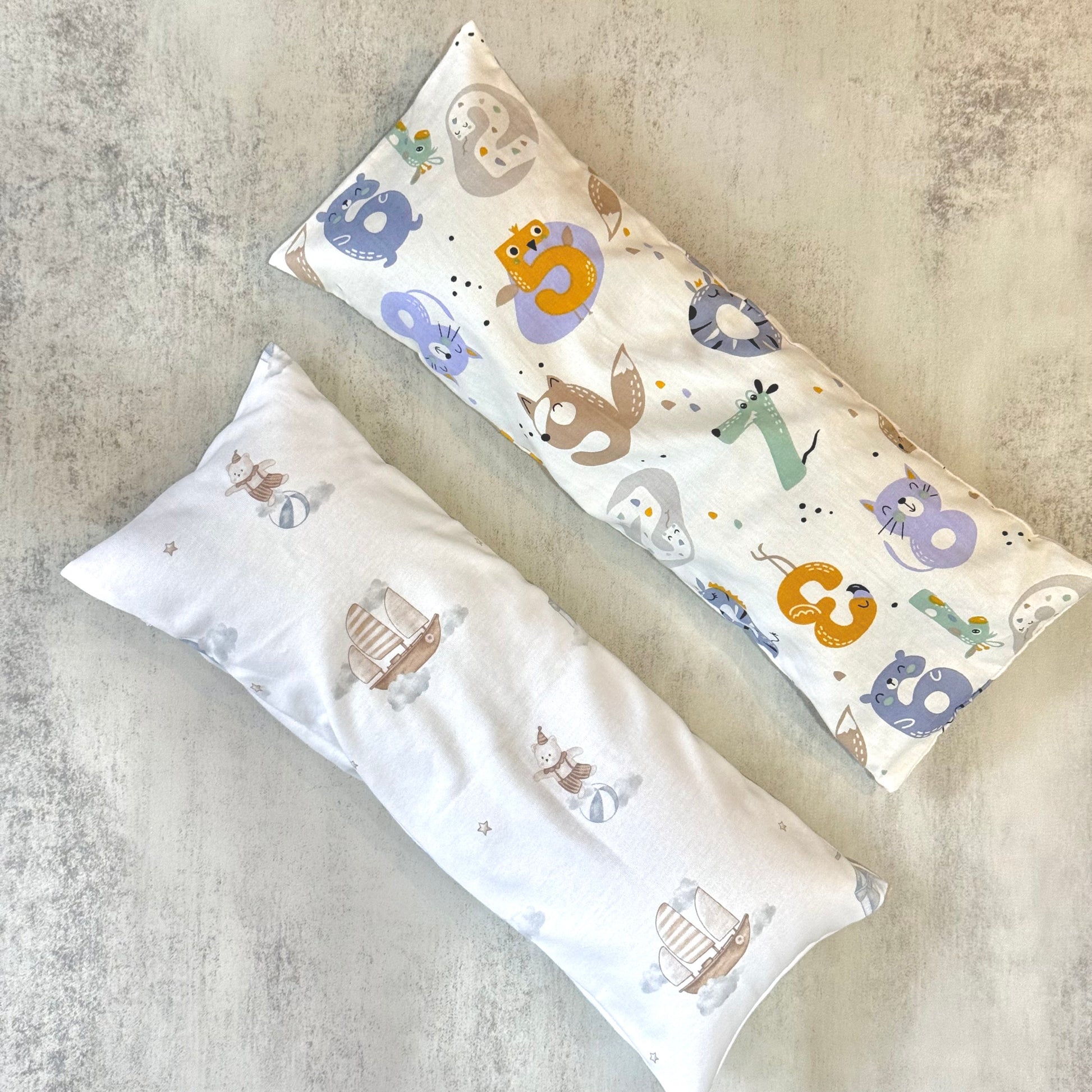 Two long, rectangular beansprout husk pillows with animal patterns on a textured surface