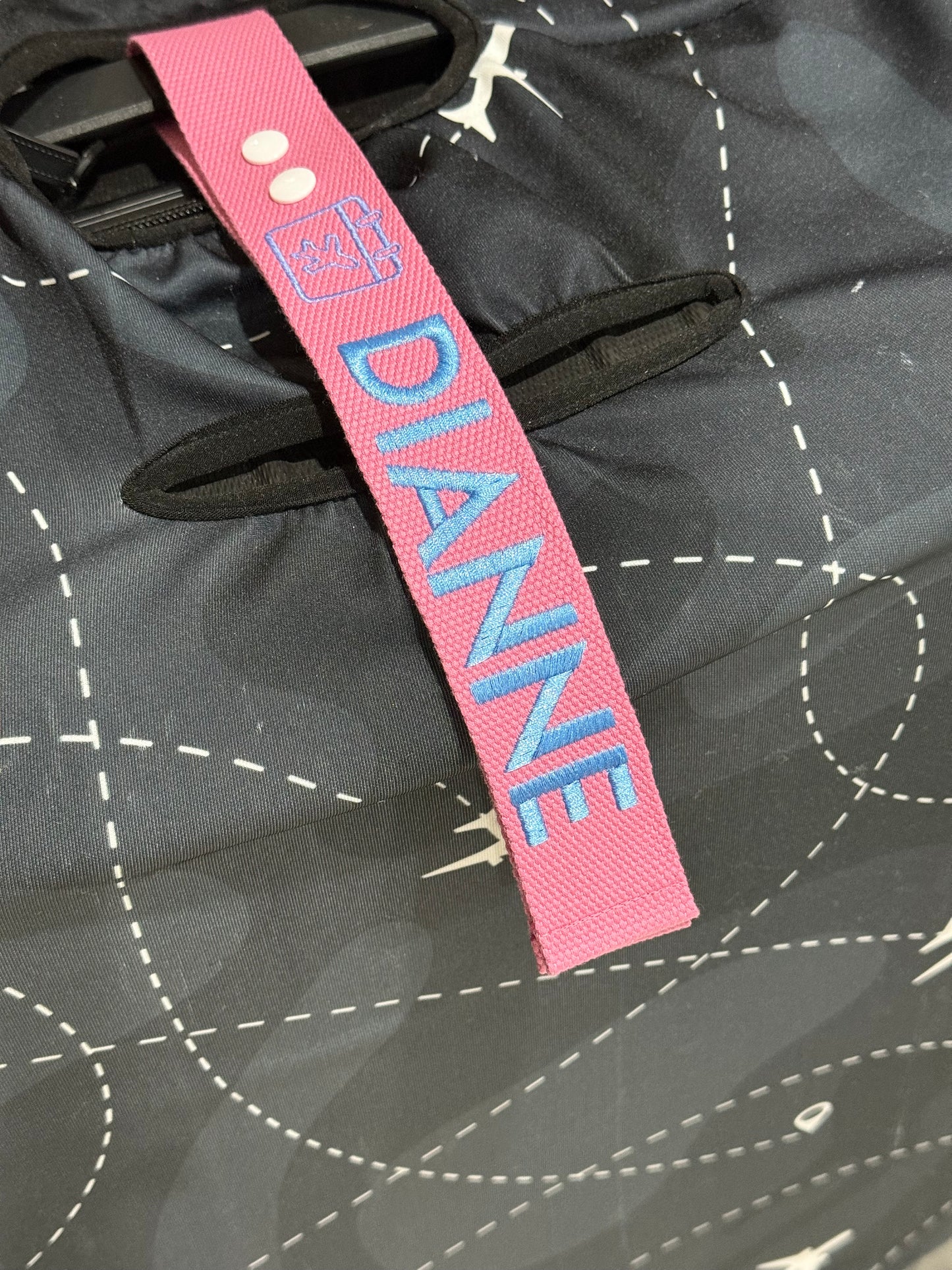 Pink luggage tag with 'DIANNE' on a black luggage