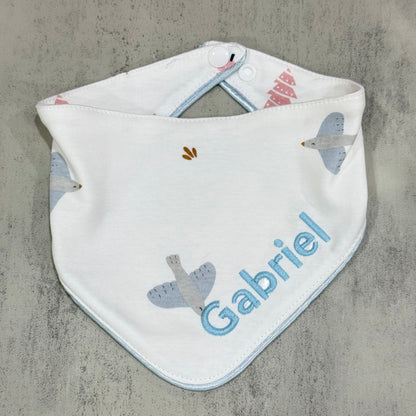 Baby bib with airplane pattern and 'Gabriel' embroidered on a concrete surface