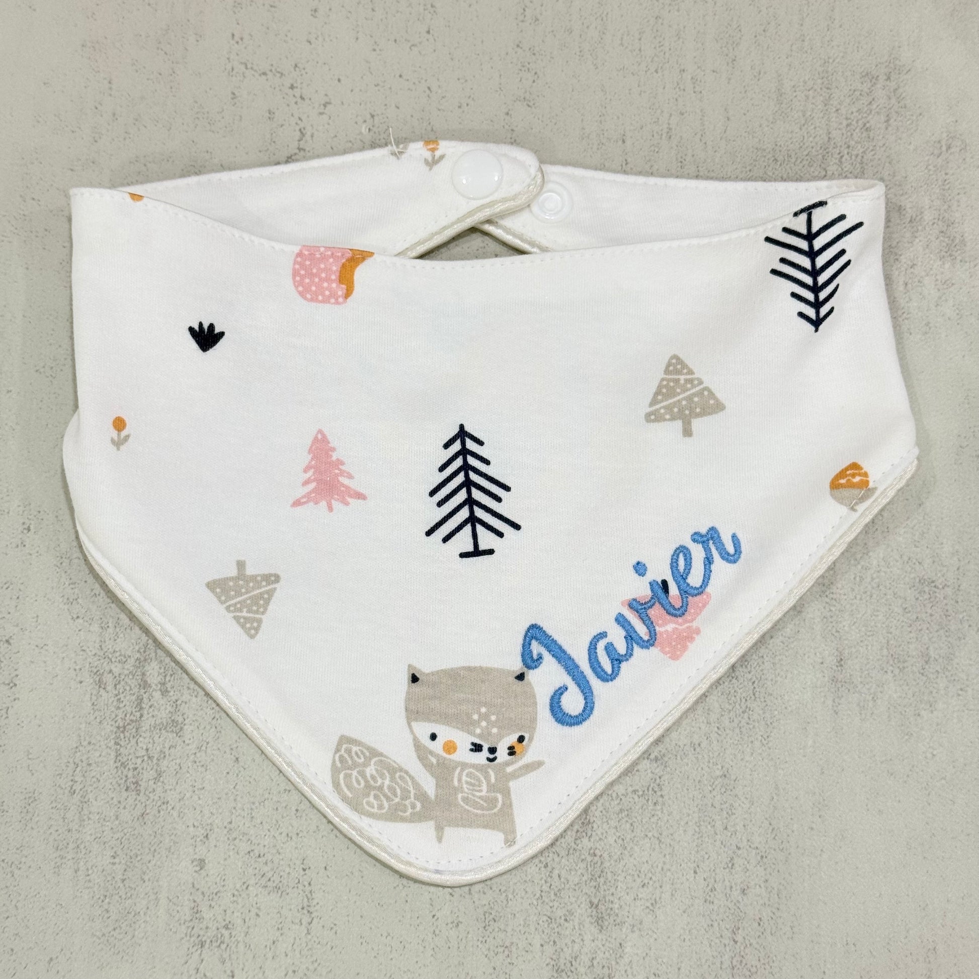 Baby bib with forest-themed patterns and the name 'Javier' on a gray background