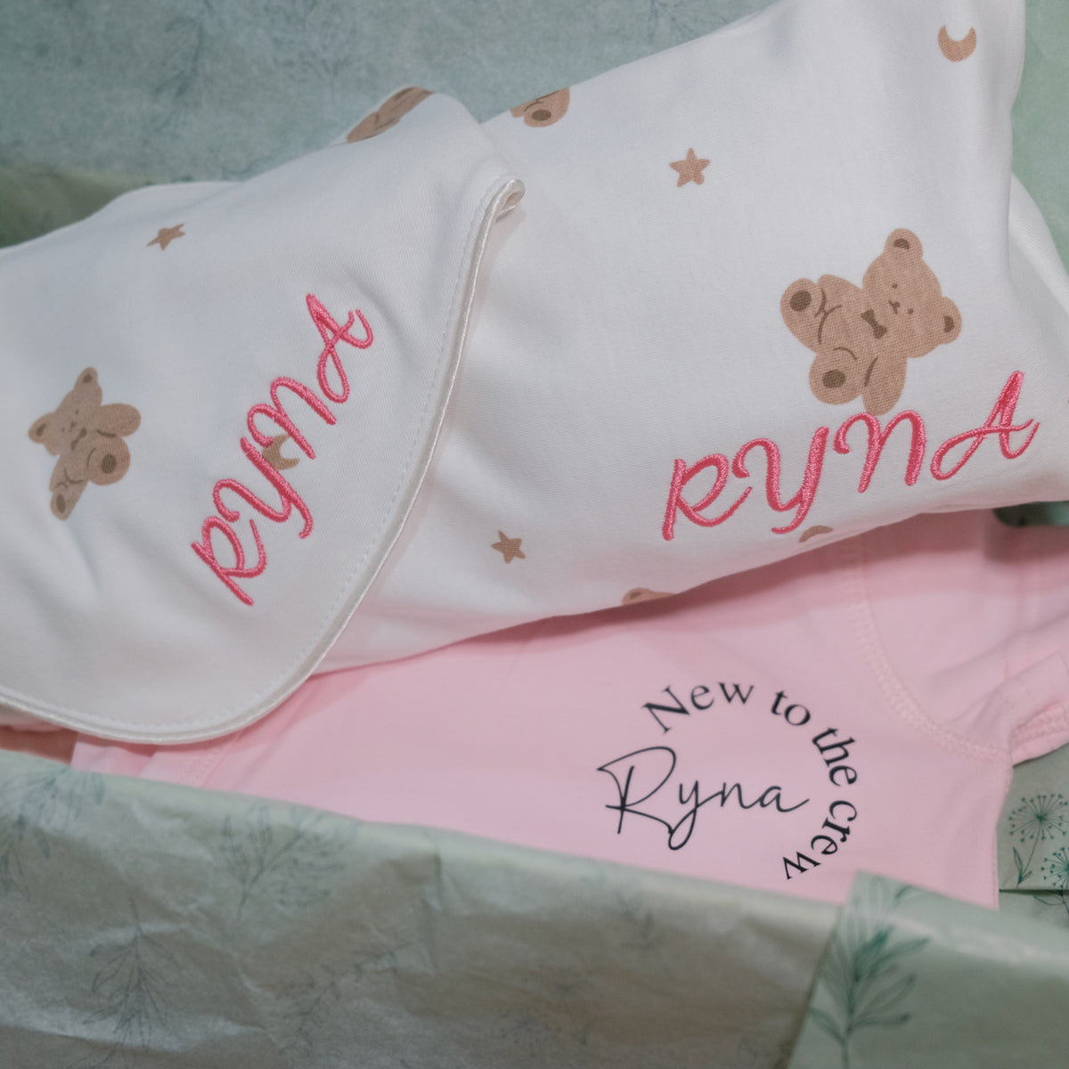 Teddy bear print pillow and bib embroidered with Ryna in pink, with a pink bodysuit